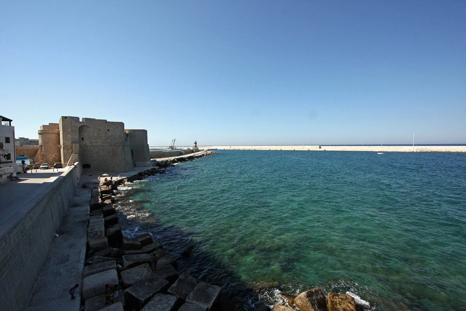 Il Castello di Carlo V in pietra chiara sul lungomare di Monopoli, con la scogliera e l'acqua turchese all'imbocco del porto